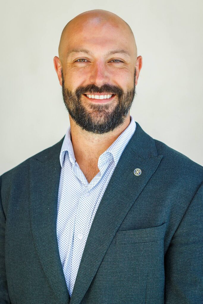 A professional executive headshot of a smiling man with a shaved head and trimmed beard wearing a dark suit jacket and white button-down shirt, captured by a Templeton business photographer.