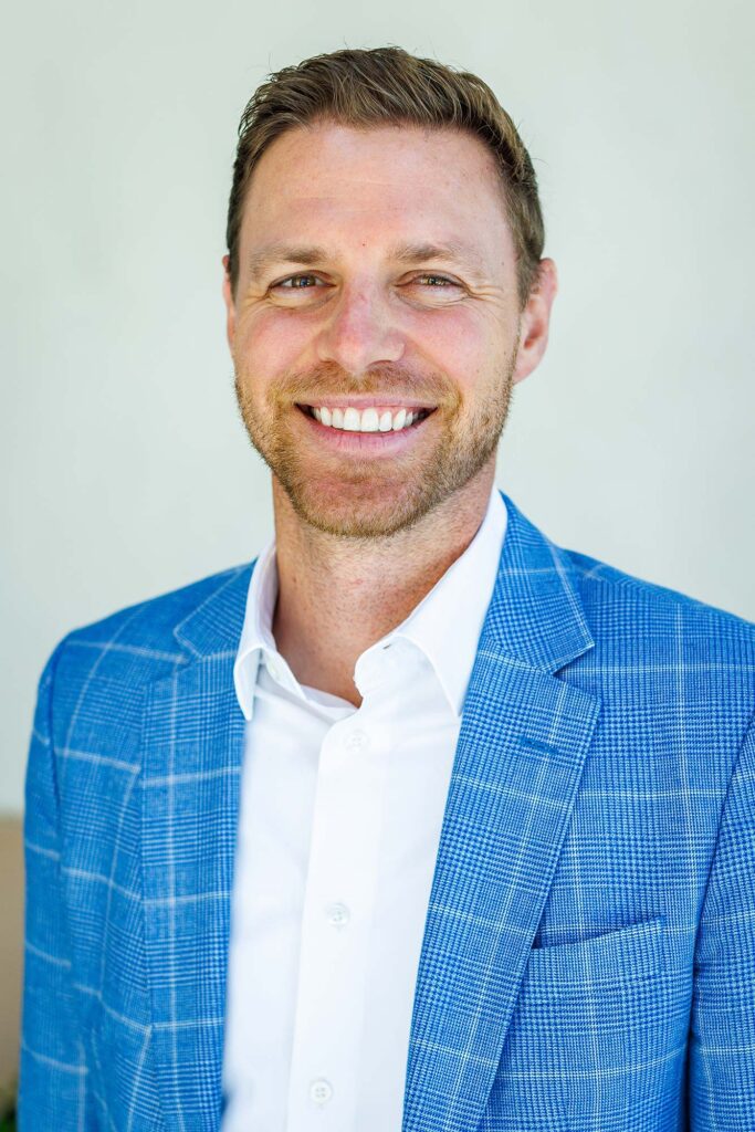A professional business headshot of a man smiling in a vibrant blue plaid blazer and white button-down shirt, taken by a corporate headshot photographer in Templeton.