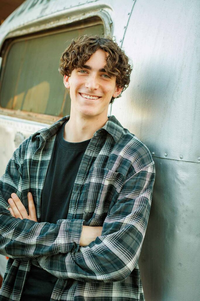 Rustic outdoor high school senior portrait of a young man smiling by an airstream trailer, shot by Paso Robles senior photographer David Pascolla