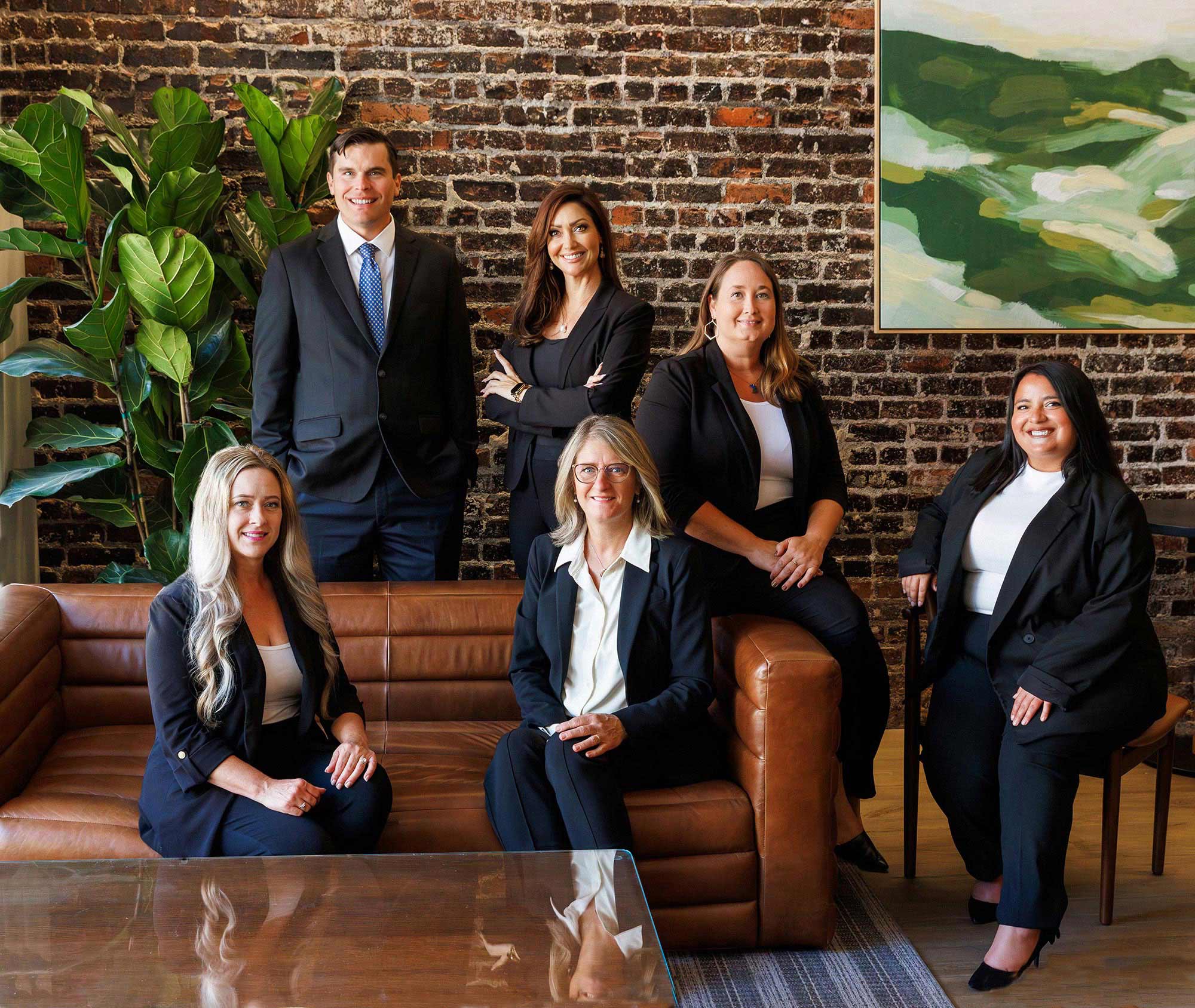 Professional corporate group portrait of an executive team posed on a leather sofa against an exposed brick wall.