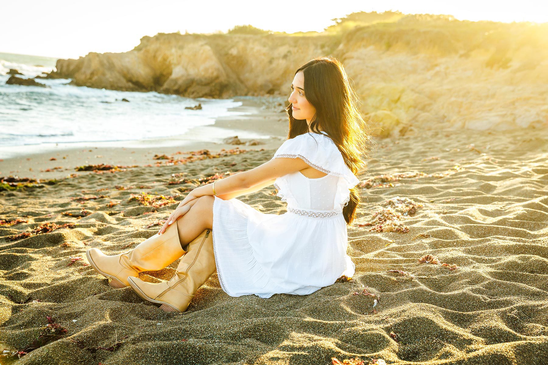 Relaxed senior graduation portrait of a girl sitting on the sand at Moonstone Beach during golden hour.