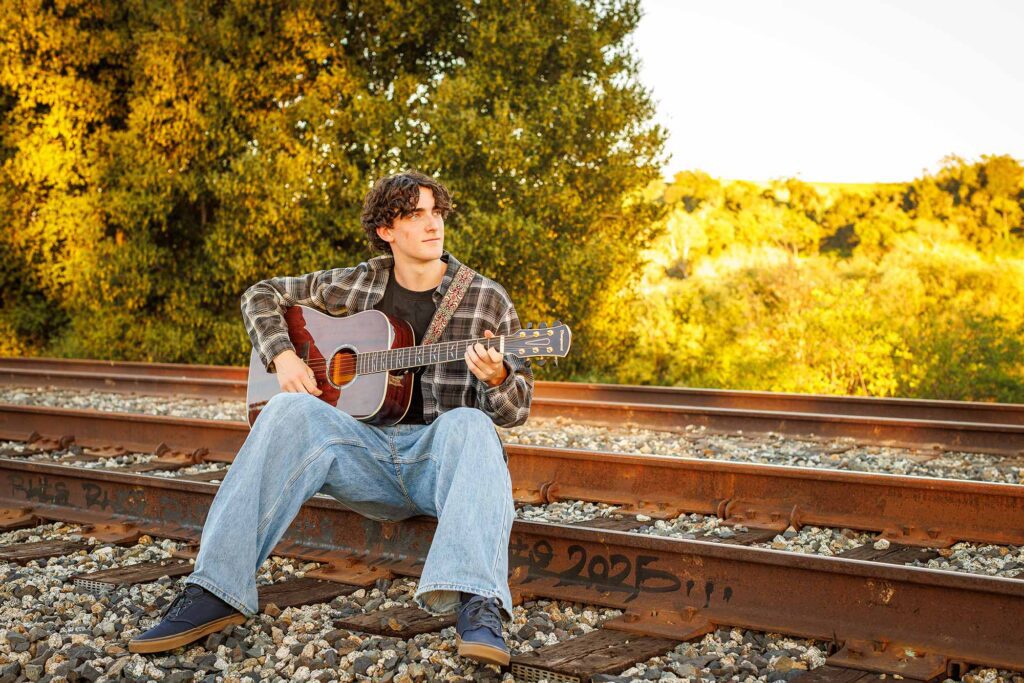 High school senior portrait of a young man with a guitar on train tracks, taken during golden hour by Paso Robles photographer David Pascolla.