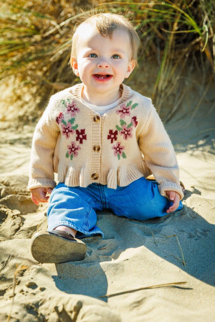 Smiling baby sitting on the sand during a family photography session in Morro Bay