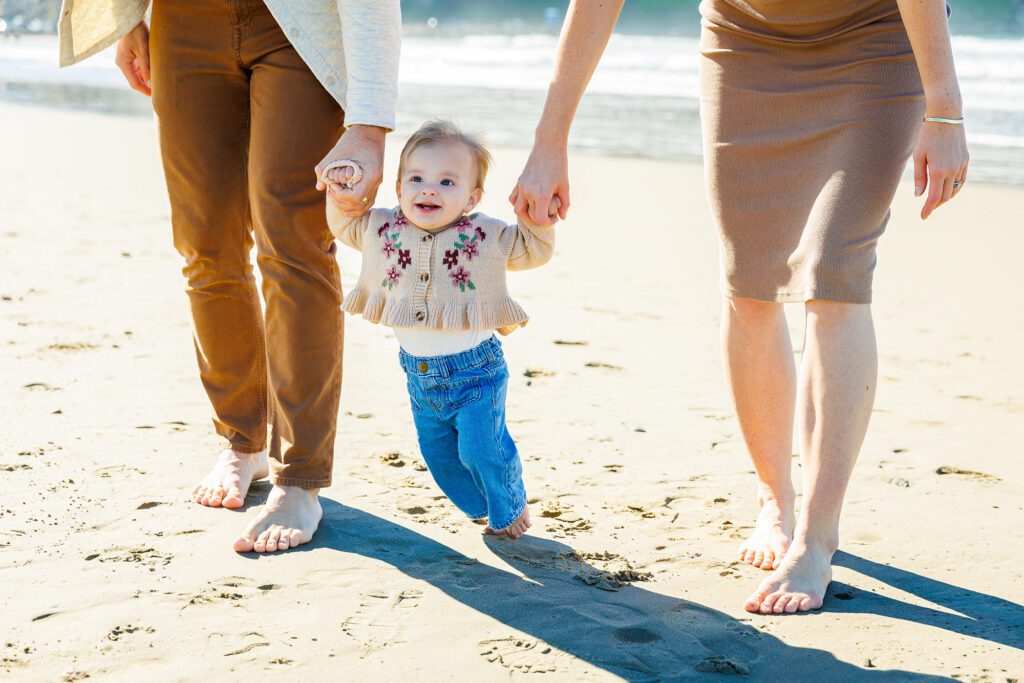 Baby walking hand in hand with parents along the beach in Morro Bay