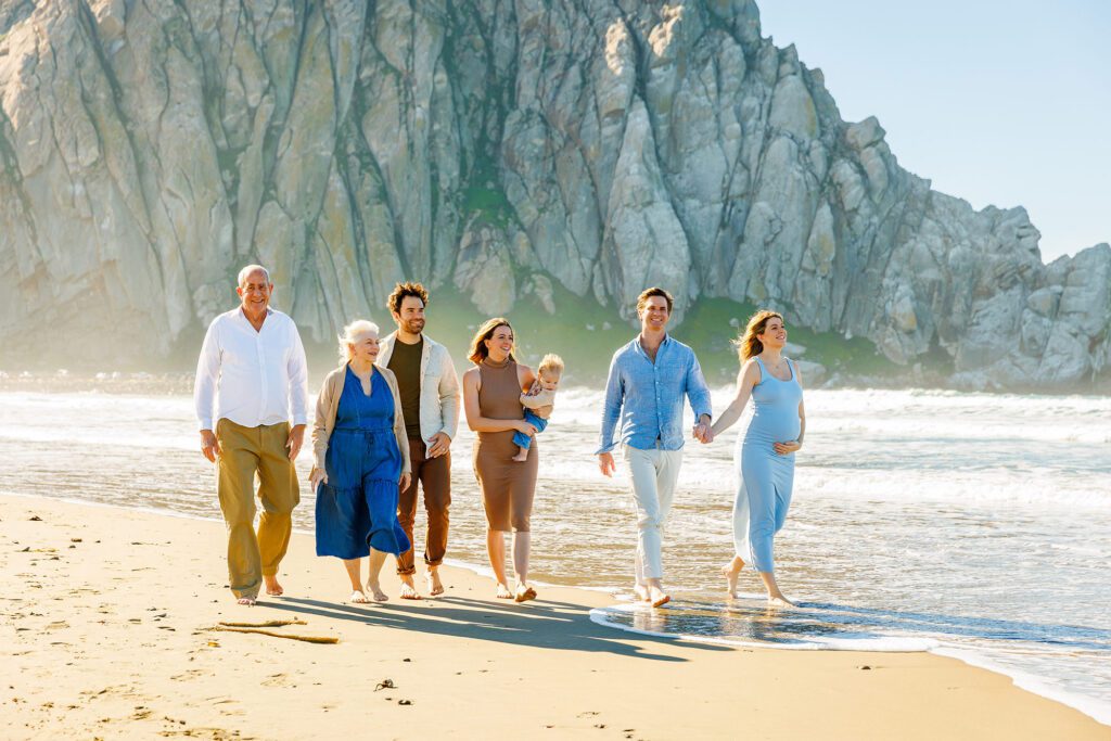 Multigenerational family walking together along the beach with Morro Rock behind them